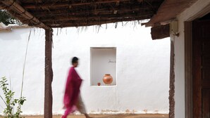 A traditional building with a thatched roof, a white exterior, and a window with a pot.