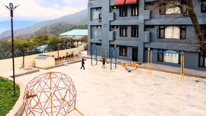 A building with multiple floors, outdoor play area, and a view of the surrounding landscape. -  Shivraj Hotel Mussoorie (Mussoorie)