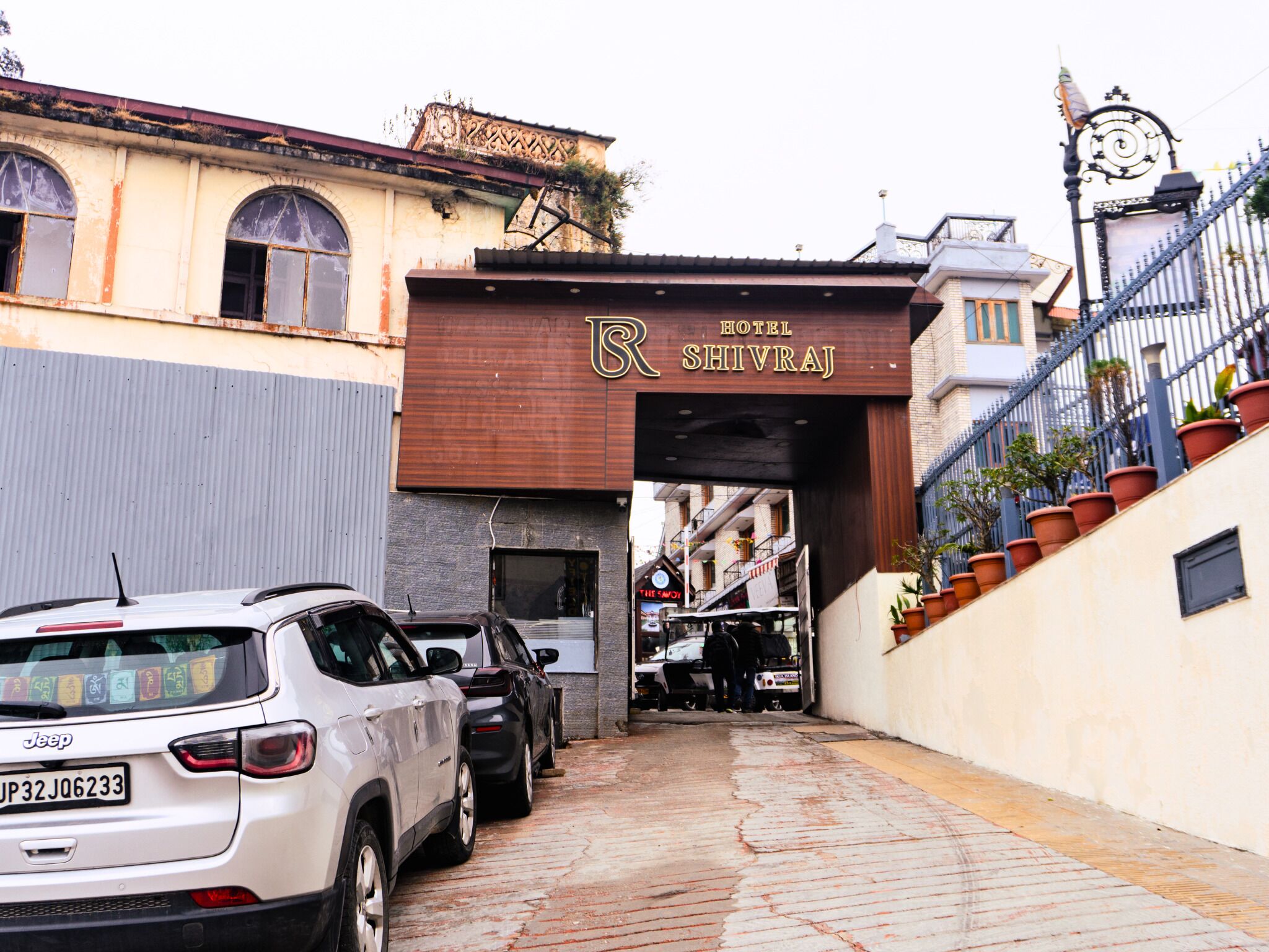 A narrow street leading to Hotel Shivraj with parked cars and a staircase on the right.