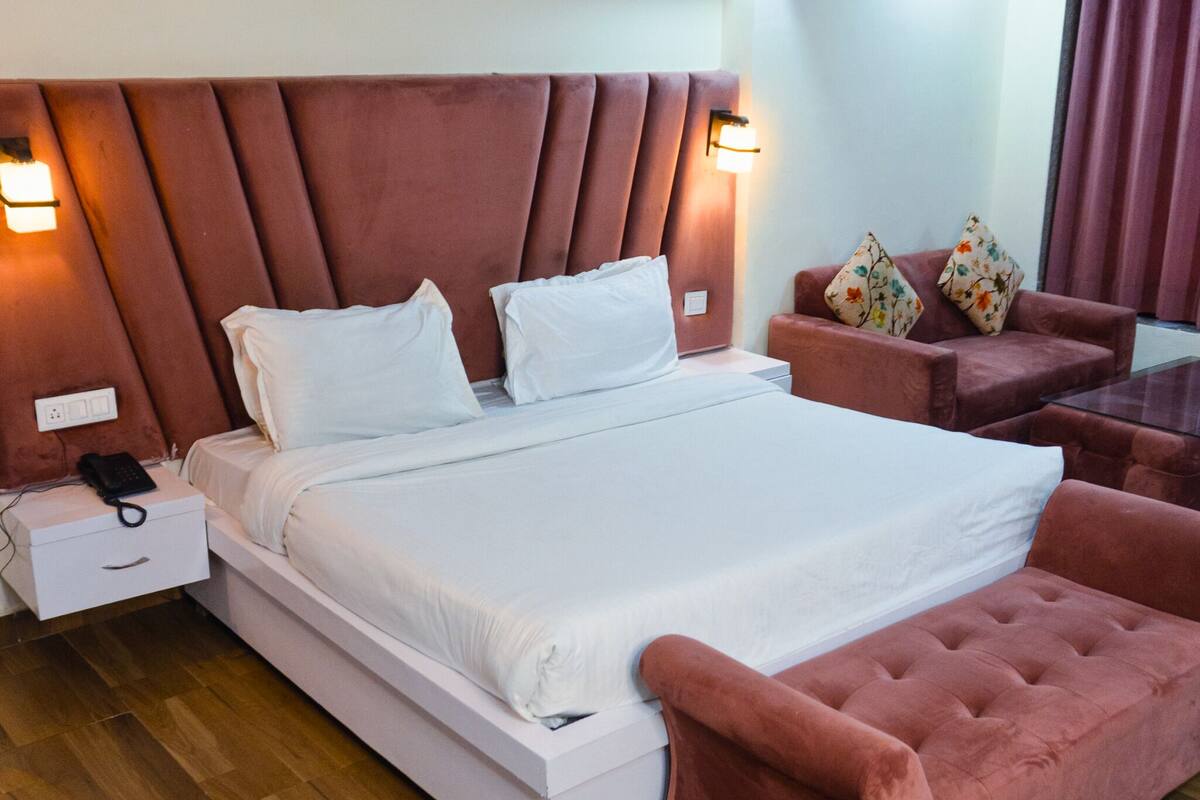 Hotellihuone, jossa on sänky, yöpöytä, puhelin, tuoli ja sohva.