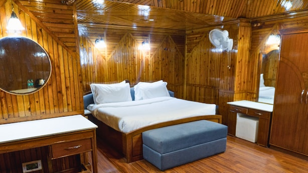 A wooden-paneled room with a bed, bedside table, bench, and a mirror. -  Shivraj Hotel Mussoorie (Mussoorie)