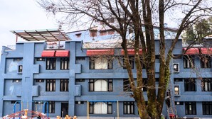 A multi-story building with a blue facade, a red awning, and a tree in the foreground. -  Shivraj Hotel Mussoorie (Mussoorie)