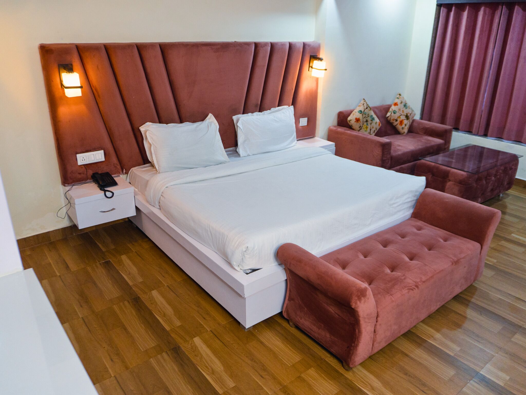 Ein modernes Hotelzimmer mit einem großen Bett, einem Nachttisch, einer kleinen Sitzecke und einem Hocker.