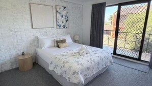 A bedroom with a bed, a nightstand, a window with a view, and artwork on the wall.