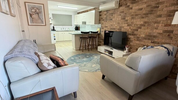 A living room with a sofa, a TV, and a kitchen in the background.