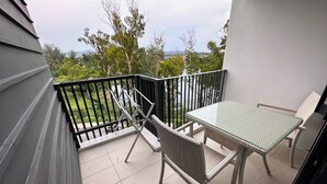 Un balcon avec une table et des chaises, une vue sur la verdure et les bâtiments, et un sol carrelé.