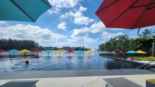 Une piscine agrémentée de parasols colorés, de chaises longues et surplombée d’un ciel dégagé.