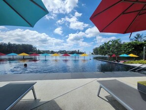 Une piscine agrémentée de parasols colorés, de chaises longues et surplombée d’un ciel dégagé.