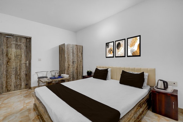 A bedroom with a bed, a wooden wardrobe, a nightstand, a coffee maker, and three framed artworks on the wall.