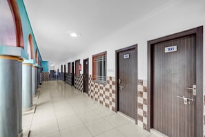A hotel corridor with numbered doors, check-in counters, and a tiled floor.