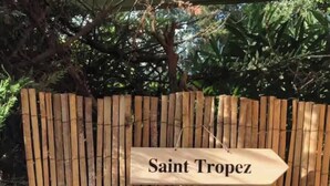 Un cartello di legno con la scritta 'Saint Tropez', un oggetto sferico colorato su una base in legno e un recinto in bambù sullo sfondo.
