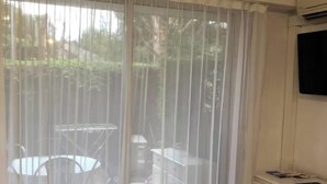 Una camera da letto con un letto, una televisione a parete, una scrivania con una sedia e vista attraverso una tenda leggera.