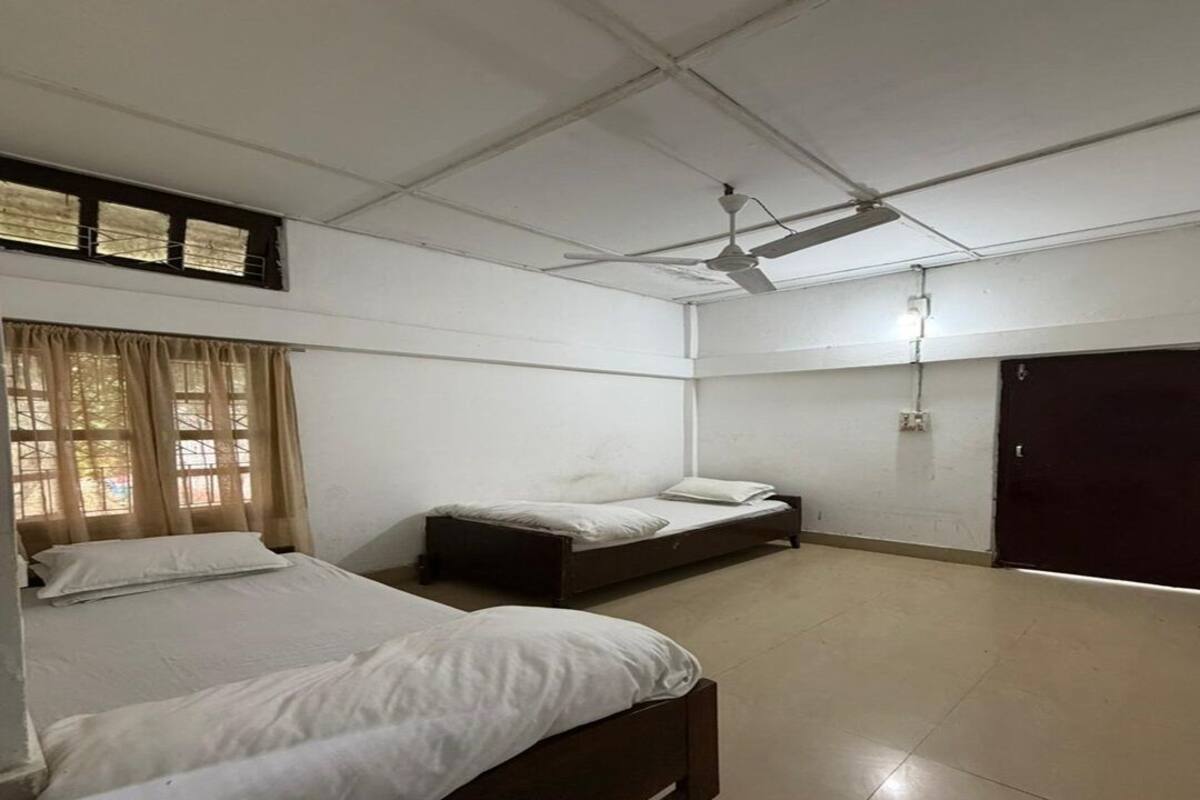 A room with two beds, a ceiling fan, a window with curtains, and a door.