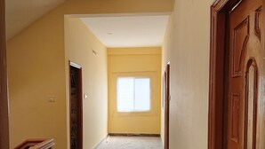 A hallway with a marble floor, a wooden door on the right, and a window at the end.