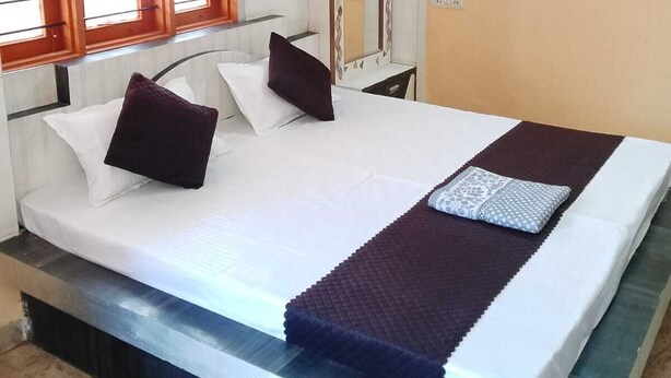 A room with a bed, a window with blinds, a mirror, and a wall with a decorative panel.