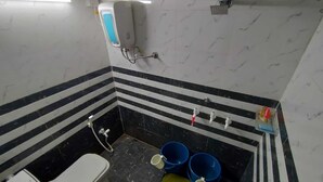 A small bathroom with a toilet, a hand dryer, and a showerhead. There are three buckets on the floor.