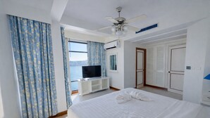 Een hotelkamer met een bed, een televisie, een plafondventilator en uitzicht op zee.