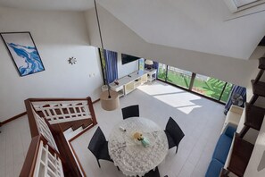 A modern interior with a dining area, a staircase, and a view of a green outdoor space. - Condo 2 BR in Laguna (Lake View) (Phuket)