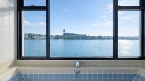Een badkamer met een bad, een raam en uitzicht op water en gebouwen.