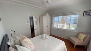A bedroom with a bed, a chair, a ceiling fan, a window with blinds, and a door leading to another room. - Dog friendly home with spectacular views of Lake Illawarra (Lake Heights)