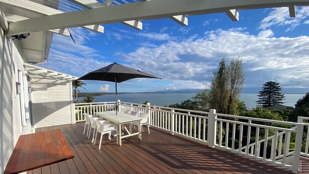 A wooden deck with a table and chairs, a black umbrella, and a white railing overlooking a body of water. - Dog friendly home with spectacular views of Lake Illawarra (Lake Heights)