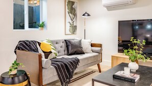 Ein modernes Wohnzimmer mit grauem Sofa, einem Flachbildfernseher, einem Couchtisch und einem Fenster mit Blick.
