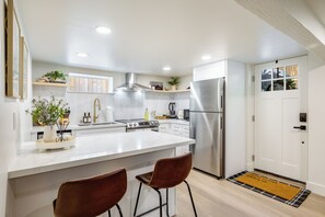 A modern kitchen with white cabinetry, stainless steel appliances, and a central island with two bar stools. - AC / New Remodel / In-Unit Laundry / Cap Hill (Seattle)