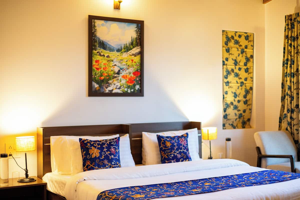 Une chambre d’hôtel avec un lit, deux lampes de chevet, une chaise, un tableau au mur et une fenêtre avec des rideaux.