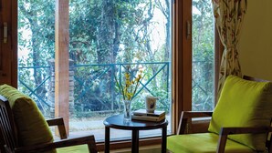 A room with a large window, two chairs, a small table with a vase, and a bed. - Alaya Stay Hill Home Petfriendly Cottage (Kosiyakutoli)