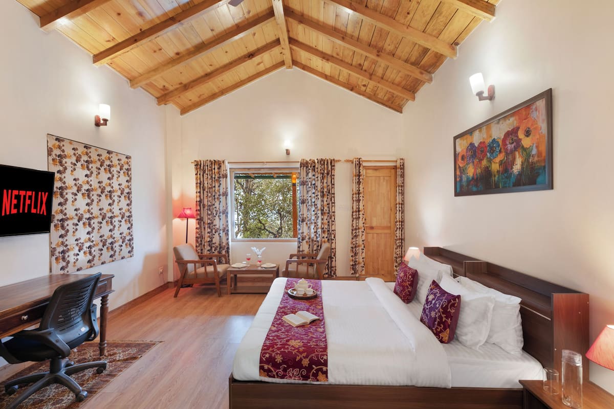 Une chambre d’hôtel avec un plafond en bois, un lit avec du linge de maison blanc, un bureau avec une chaise, une télévision et un tableau accroché au mur.