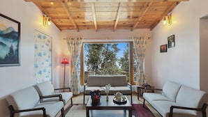 A room with a wooden ceiling, a sofa, a coffee table with a tray, a lamp, and a view through a window. - Alaya Stay Hill Home Petfriendly Cottage (Kosiyakutoli)