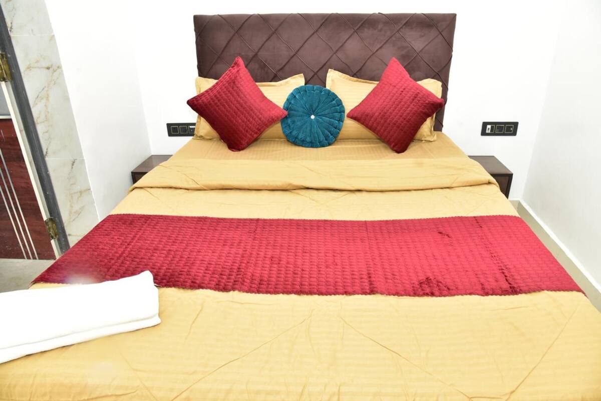 A bed with a brown headboard, two red pillows, a blue accent pillow, and a red blanket.