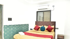 A bedroom with a bed, a bedside table, an air conditioning unit, and a window. - Hotel Emirates Case (Raipur)