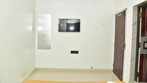 A room with a white wall, a mounted television, a door with a decorative handle, and a tiled floor. - Hotel Emirates Case (Raipur)