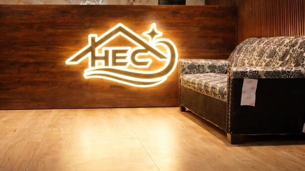 A reception area with a wooden reception desk, a logo illuminated in the center, a patterned sofa, and a marble wall. - Hotel Emirates Case (Raipur)