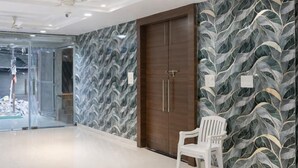 A spacious room with a large wardrobe, a white chair, and a patterned wall. - Hotel Emirates Case (Raipur)