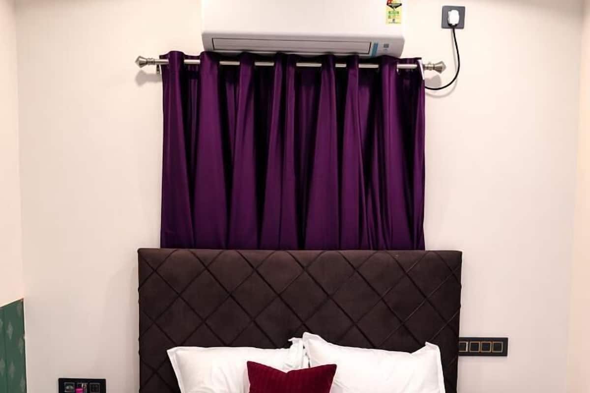 A neatly made bed with white and maroon bedding, a dark headboard, and purple curtains.