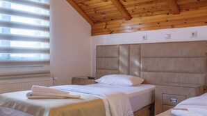 A room with two beds, wooden ceiling beams, a radiator, and a window with blinds.