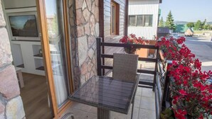 A balcony with wicker furniture, a stone wall, and red flowers.