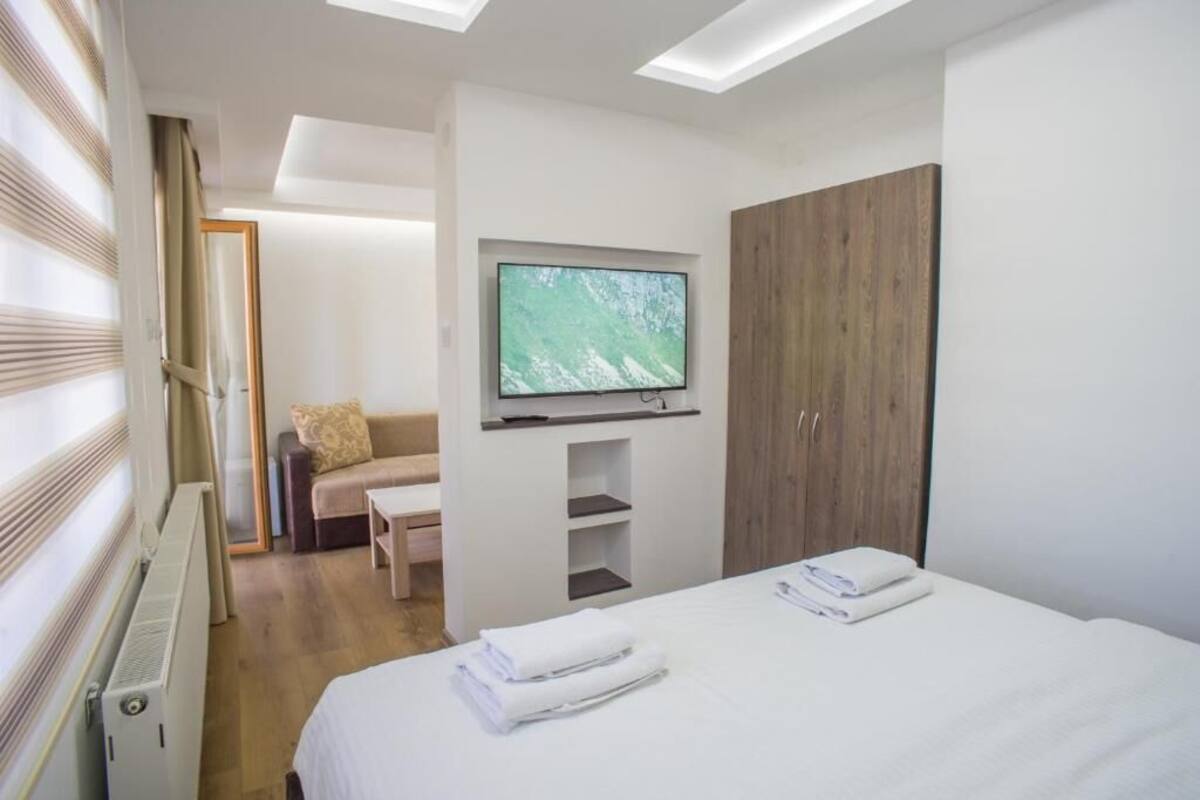 Une chambre d’hôtel moderne équipée d’un lit, d’un téléviseur fixé au mur, d’une armoire en bois et d’un coin salon avec un canapé et une table.