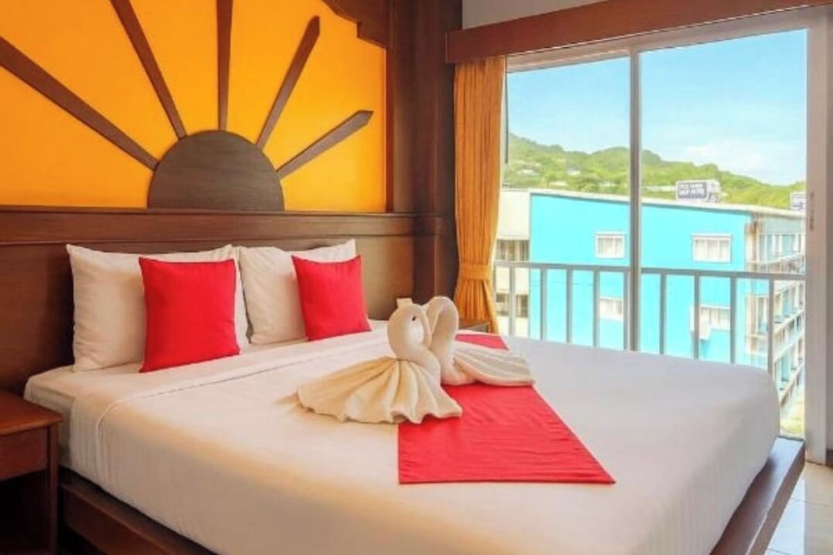 Habitación de hotel con una cama grande, un adorno en la pared con forma de sol, vistas a la ciudad y un balcón.
