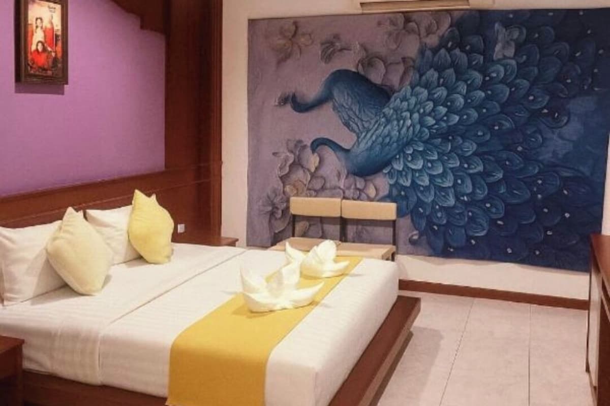 Una habitación de hotel con una cama grande, un mural de pavo real y una mesita.
