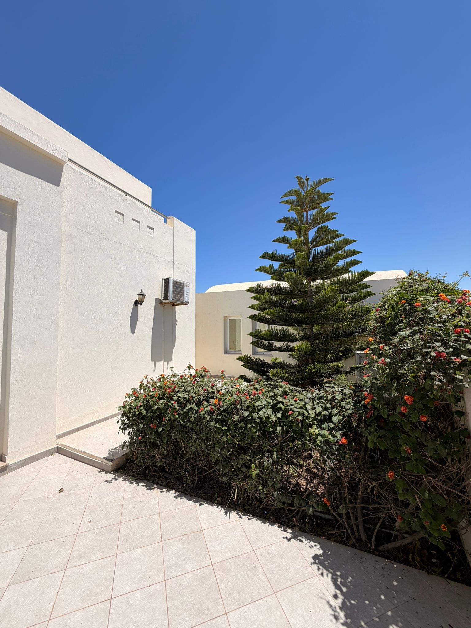 Un bâtiment à l’extérieur blanc, doté d’une petite fenêtre et d’un appareil de climatisation fixé au mur.