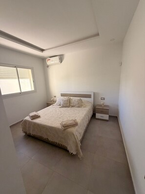 Une chambre à coucher comprenant un lit, des tables de chevet, un appareil de climatisation et une fenêtre.