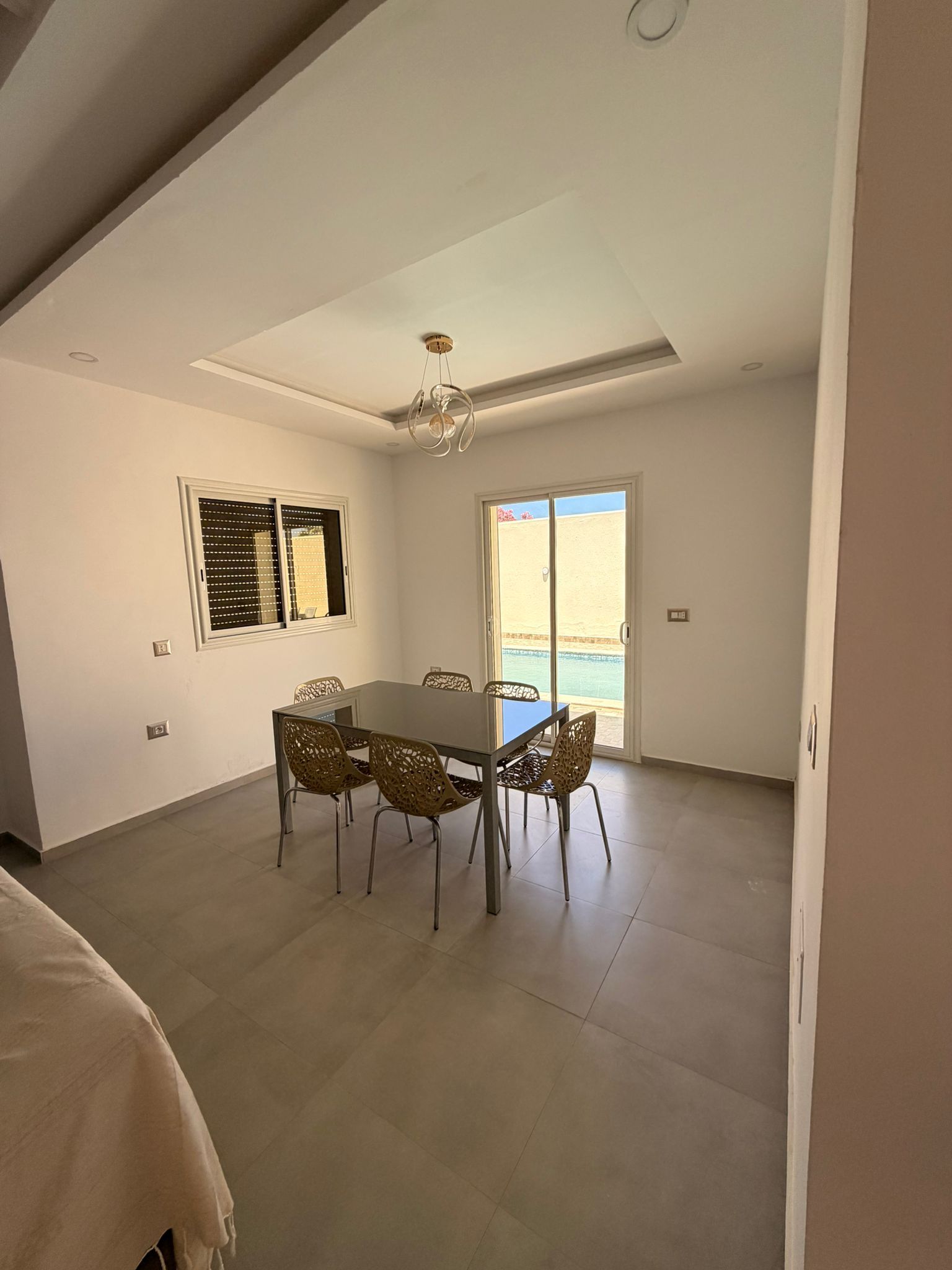 Un vaste espace dédié à la salle à manger, comprenant une table et des chaises, un luminaire au plafond, et une vue sur l’extérieur par une porte.