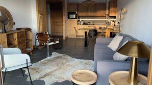 Una sala de estar moderna con sofá, mesa de centro, alfombra y un comedor con armarios de madera y televisor.