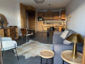 Ein modernes Wohnzimmer mit einer Couch, einem Couchtisch, einem Teppich und einem Essbereich mit Holzschränken und einem Fernseher.