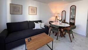 Ein modernes Wohnzimmer mit einem dunklen Sofa, einem Holztisch, einem Esstisch mit Stühlen und zwei Wandspiegeln.