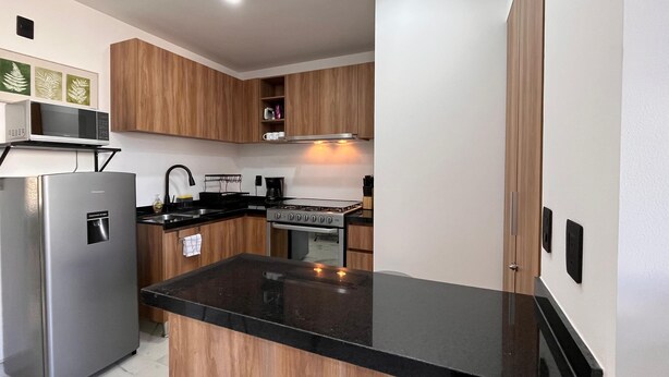 Eine moderne Küche mit Holzschränken, einem Edelstahlkühlschrank, einer schwarzen Arbeitsplatte und einem Gasherd.
