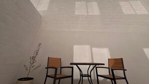 Ein Zimmer mit weißer Ziegelwand, zwei Holzstühlen, einem kleinen Tisch und einem Blumentopf.
